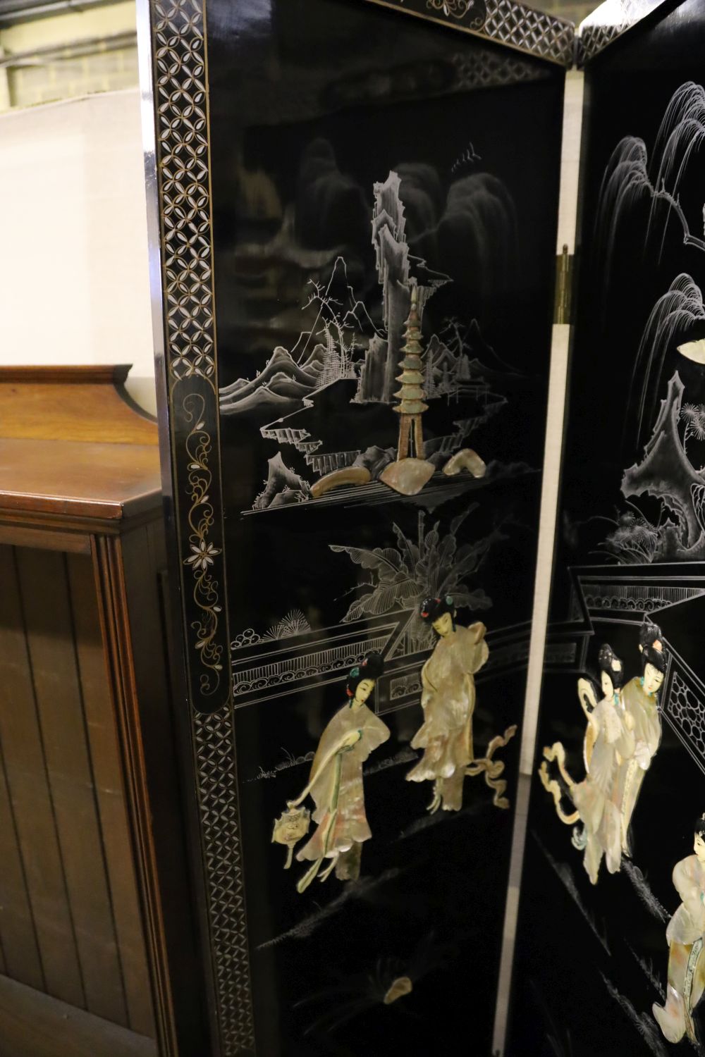 A Japanese black-lacquered and painted four-fold screen with applied decoration of geishas and temple, each panel 46 x 182cm